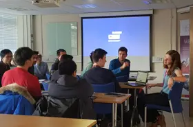 Students in classroom sat with teachers, discussing.